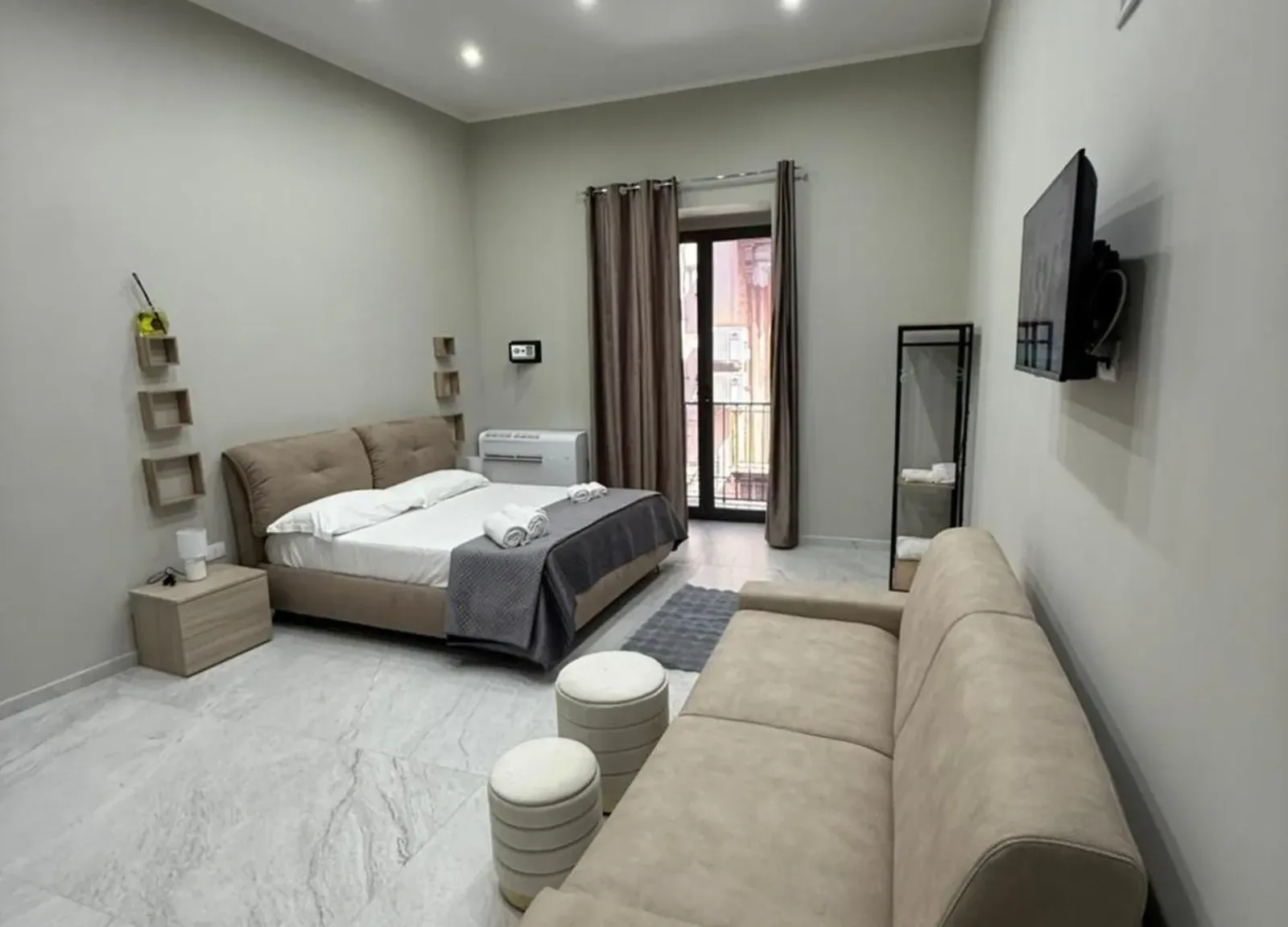 Camera dai soffitti alti con divano beige, TV e balcone