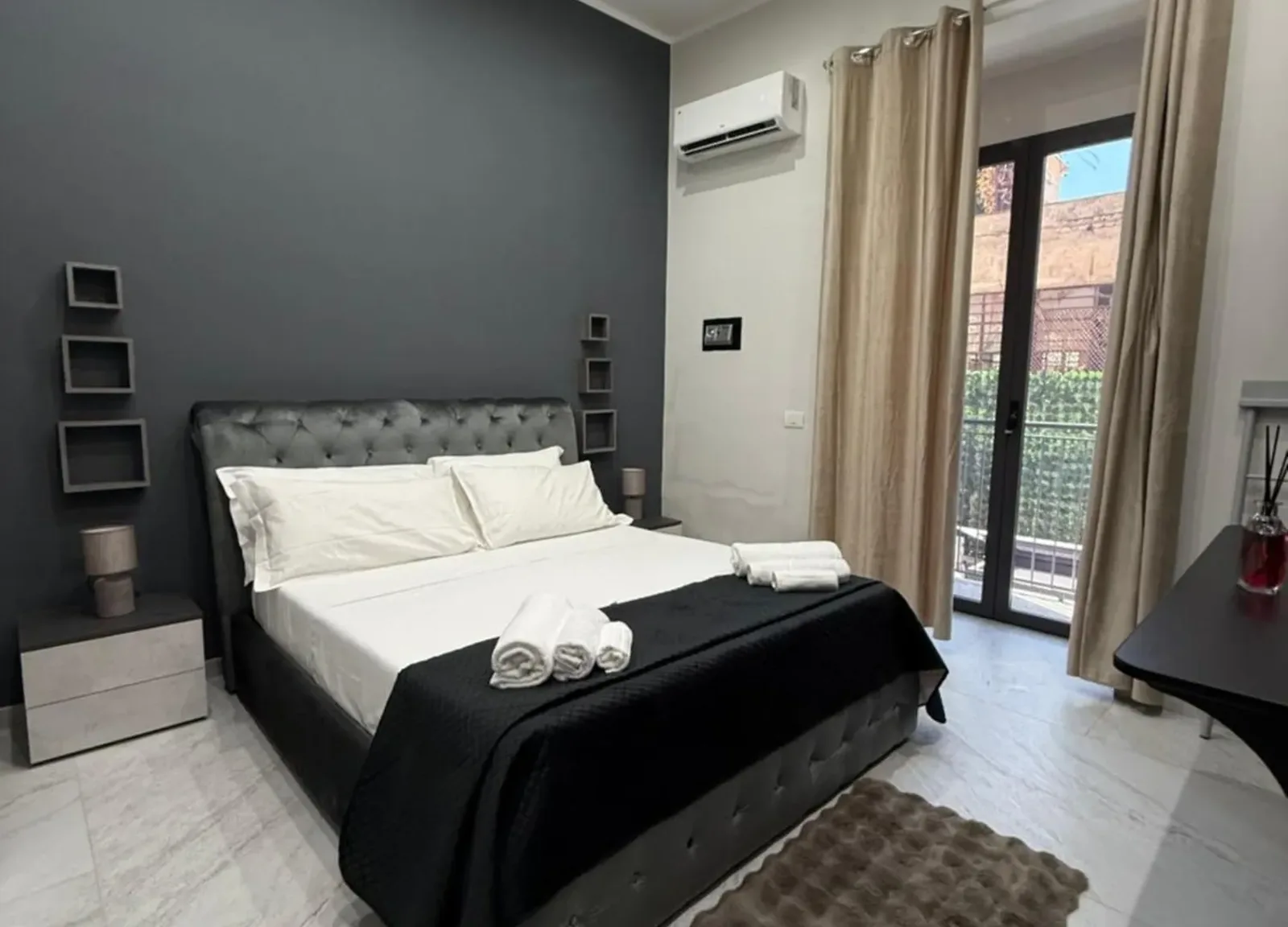 Camera con parete grigio scuro, letto capitonné e porta sul balcone