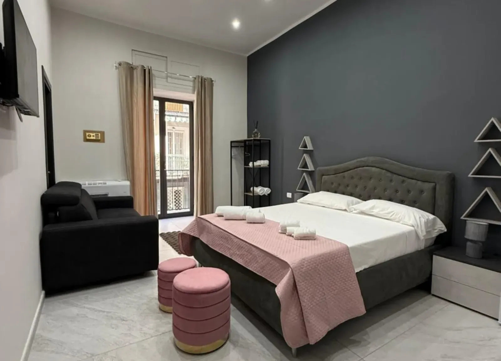 Camera con copriletto rosa, pouf abbinati e divano nero